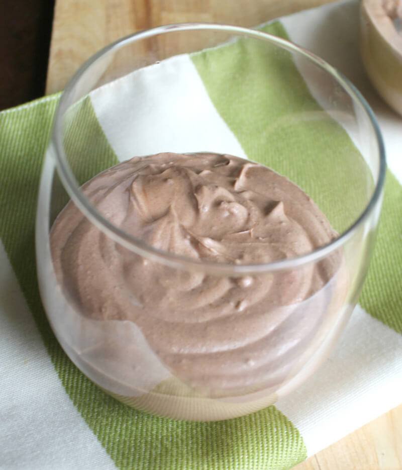 a glass with healthy paleo chocolate mousse on a striped kitchen towel