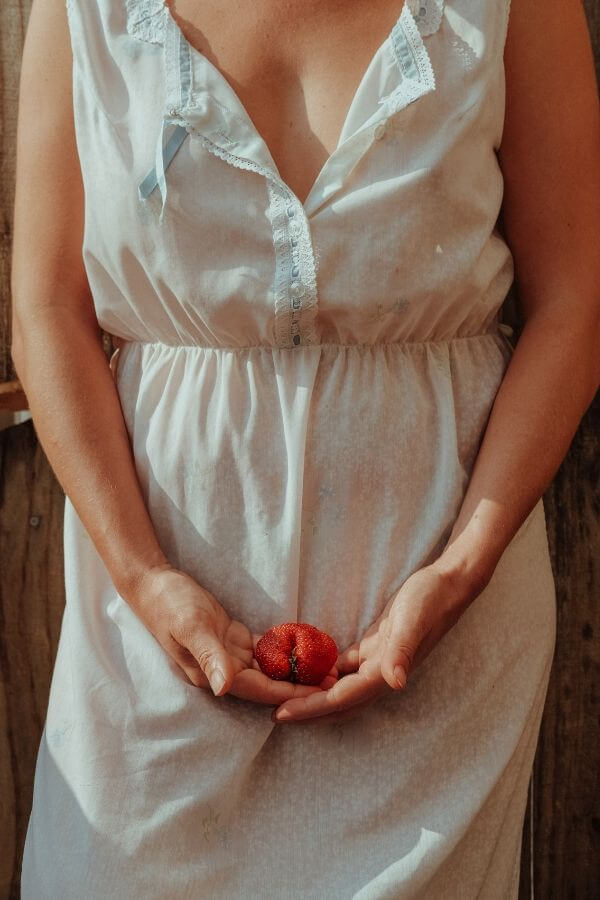 a woman in a white dress holding a strawberry