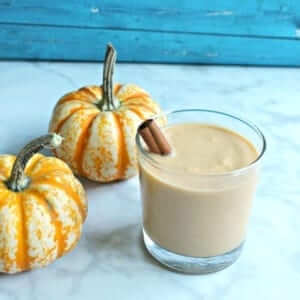 close shot of small pumpkin smoothie with cinnamon stick stirrer next to two mini pumpkins