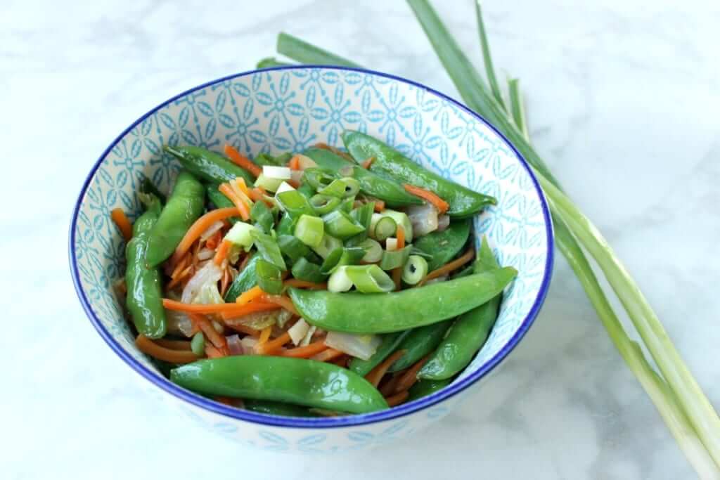 close shot of a patterned blue bowl containing edamame, green onions, carrots, and other vegetables with two sprigs of green onion