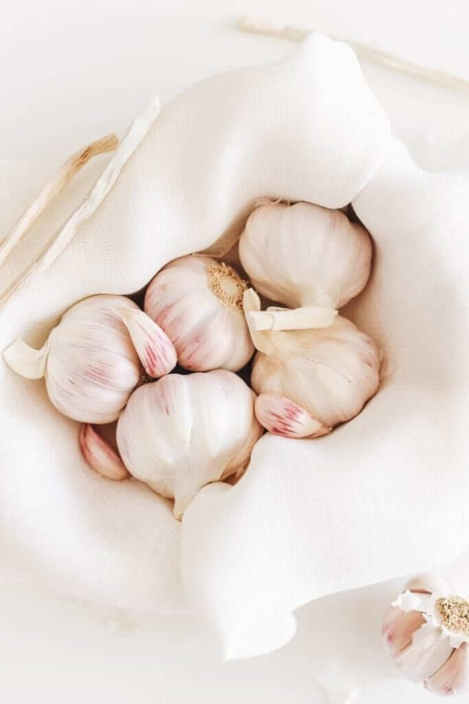 slightly pink garlic bulbs with some cloves separated in a bowl lined with a white cloth