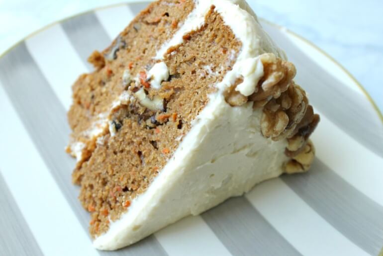 slice of carrot cake with white frosting and walnut detailing on a striped plate