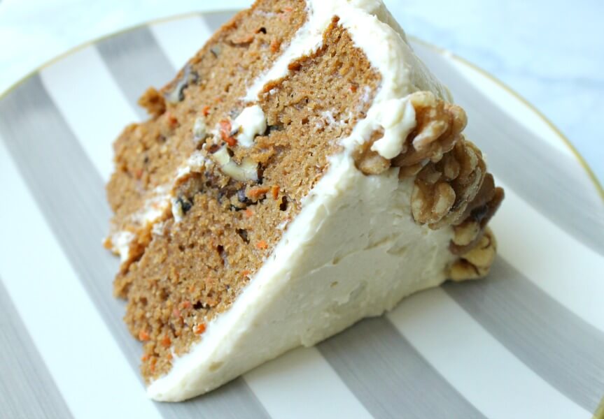 slice of carrot cake with white frosting and walnut detailing on a striped plate