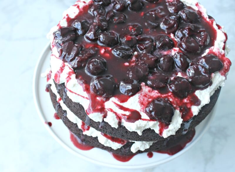 chocolate layered cake on a white plate with cherries and white frosting between layers