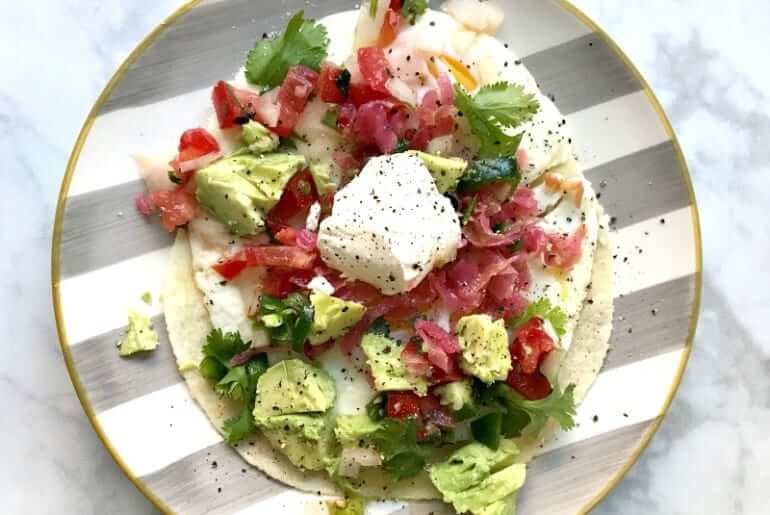 close overhead shot of an open faced taco with egg on a striped plate on a white marble countertop