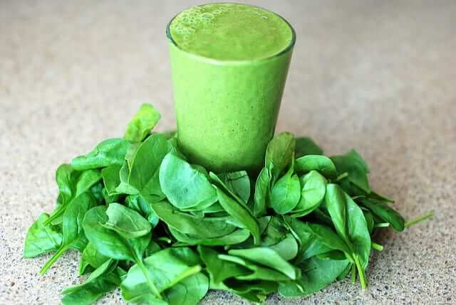 a glass of green smoothie surrounded with spinach leaves