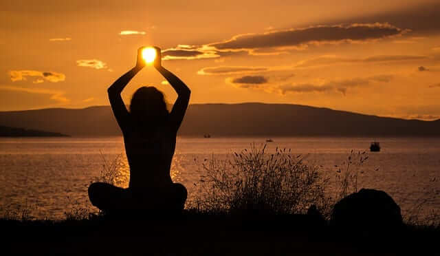 a woman doing yoga at a lake during sunset