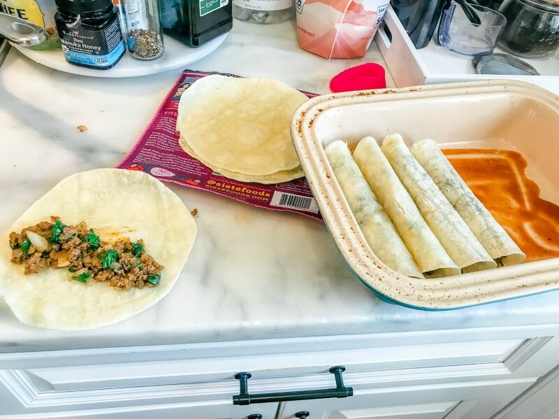 gluten-free beef enchiladas being layered in a casserole dish with gluten-free enchiladas sauce 