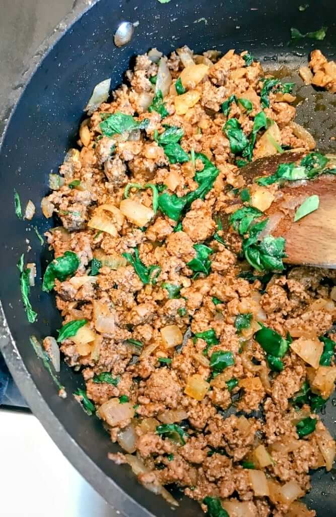 ground beef being stir-fried with spinach for making gluten-free enchiladas