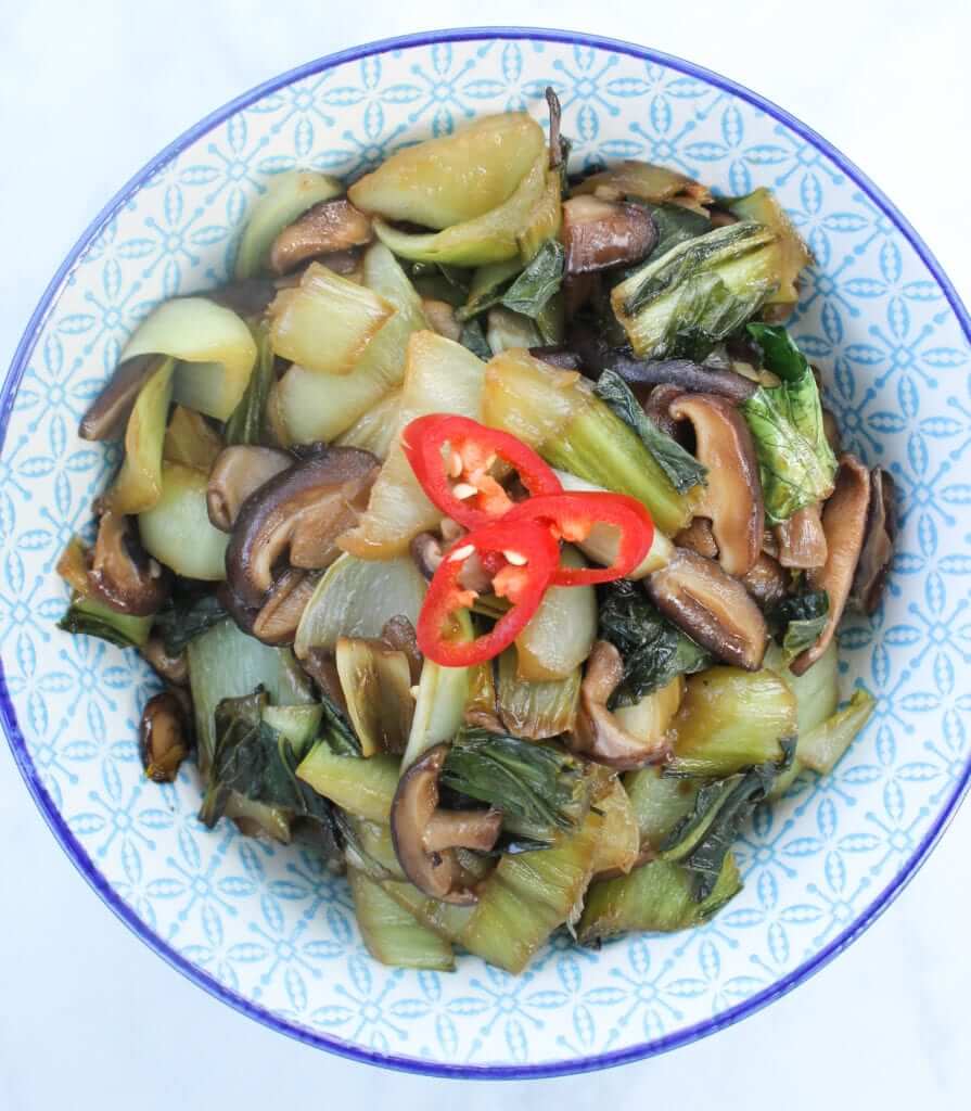 overhead shot of a bowl of keto stir-fry with shiitake mushrooms and bok choy garnished with chopped red chilies 