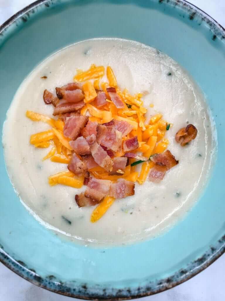 overhead shot of a bowl of paleo cauliflower potato soup topped with bacon and shredded cheddar cheese