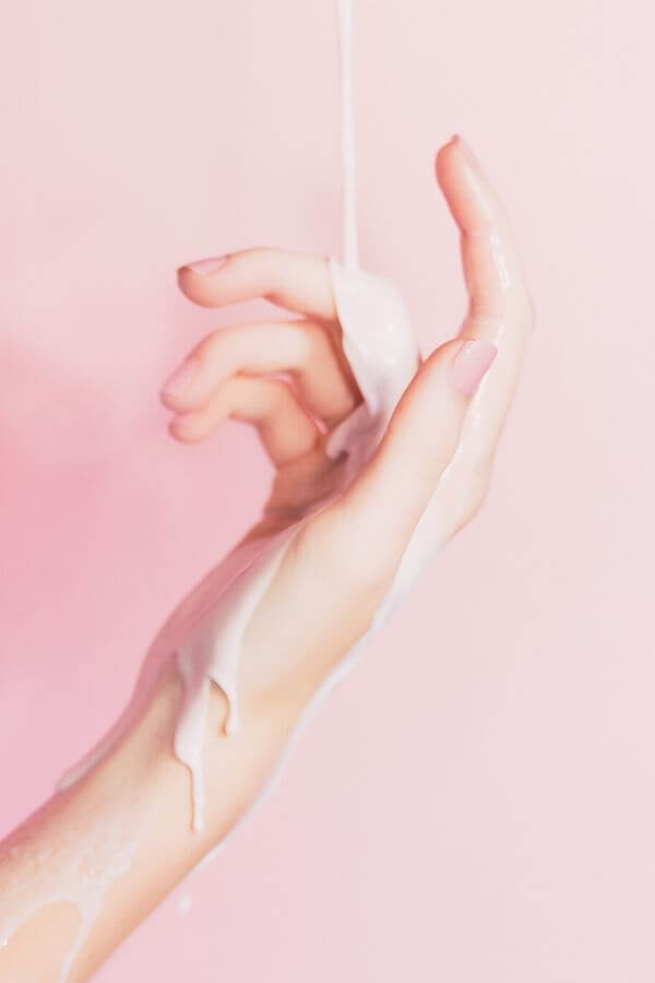 creamy body lotion running down a hand against pastel pink background