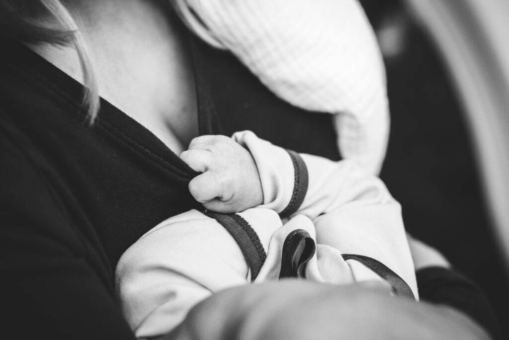 a black and white picture of a baby reaching for its mother's breast