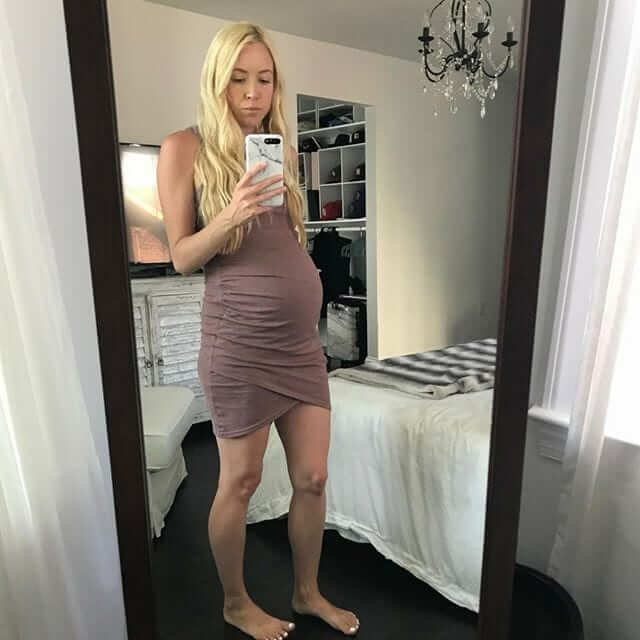 a pregnant blond woman taking a picture of herself in front of a whole body mirror