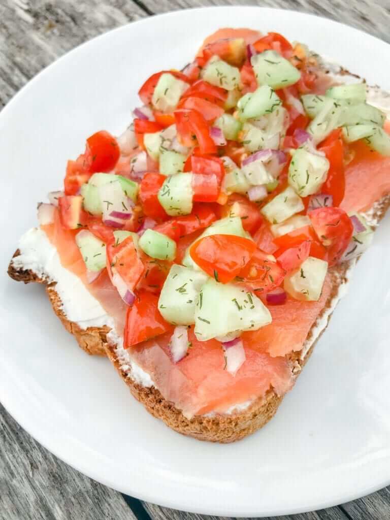 a slice of gluten-free toast spread with cream cheese, smoked salmon, tomatoes and cucumber 