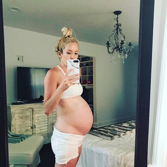 pregnant woman without stretch marks taking a picture of herself in front of a whole body mirror 