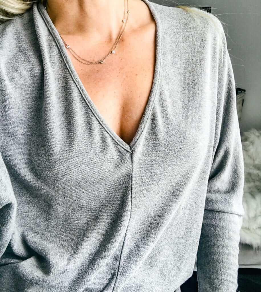 a blonde woman in a grey sweater showing off her natural looking cleavage after a breast augmentation with fat transfer 