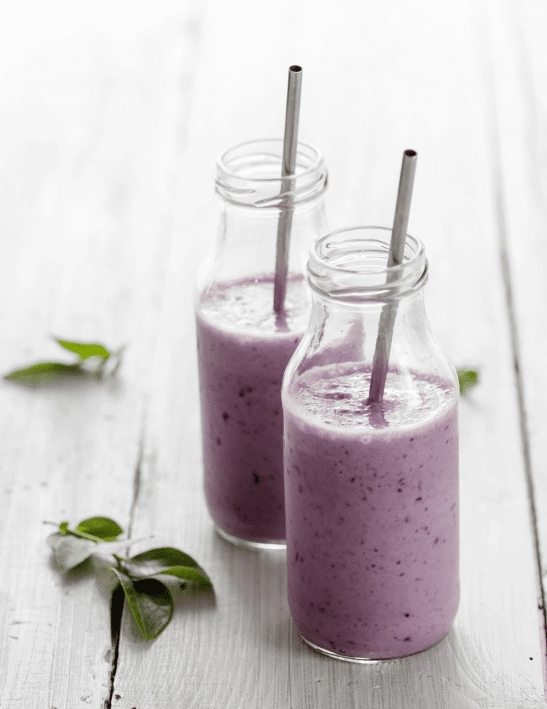 two small glass retro drinking bottles  with metal straws filled with healthy blueberry collagen smoothie